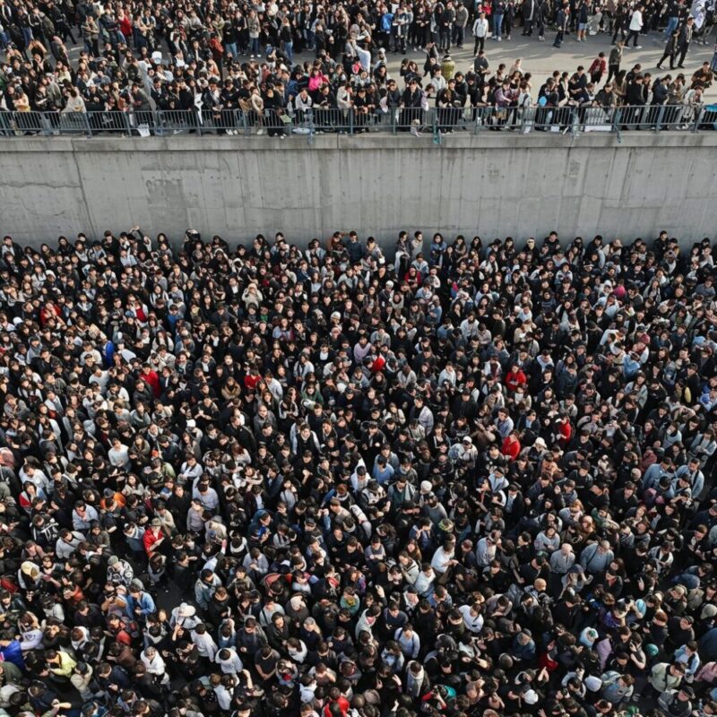 콘크리트 장벽 근처에 모인 수많은 동아시아 사람들의 거대한 군중 모습입니다.